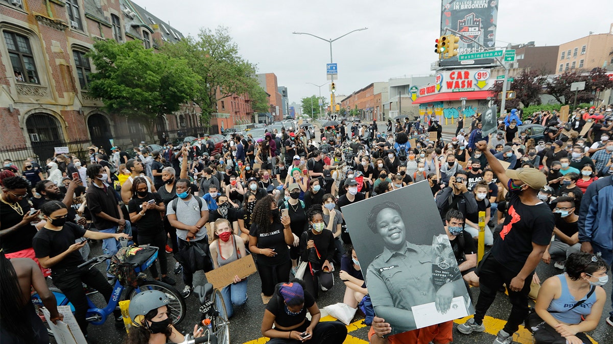 A man holds a photograph of Breonna Taylor on her birthday as he kneels with other protesters in Brooklyn during a solidarity rally for George Floyd on June 5. (AP)