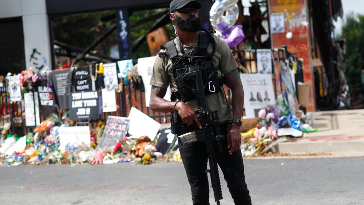 An armed protester awaits the casket of Rayshard Brooks to pass by the area where he was killed near a Wendy's restaurant on Tuesday, June 23, 2020, in Atlanta. (AP Photo/John Bazemore)