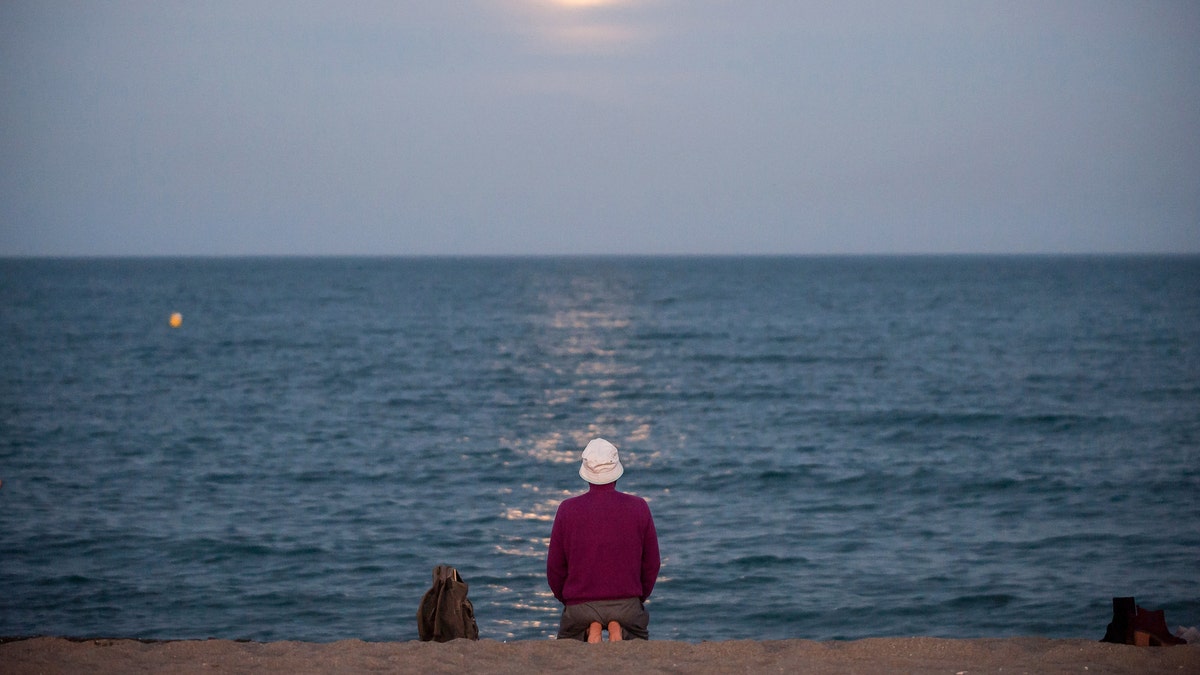 The strawberry full moon, as part of a penumbral lunar eclipse, rises over the horizon as a man sits at Malagueta beach in Spain, June 5, 2020.