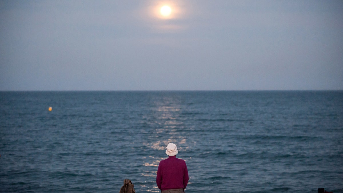 The strawberry full moon, as part of a penumbral lunar eclipse, rises over the horizon as a man sits at Malagueta beach in Spain, June 5, 2020.
