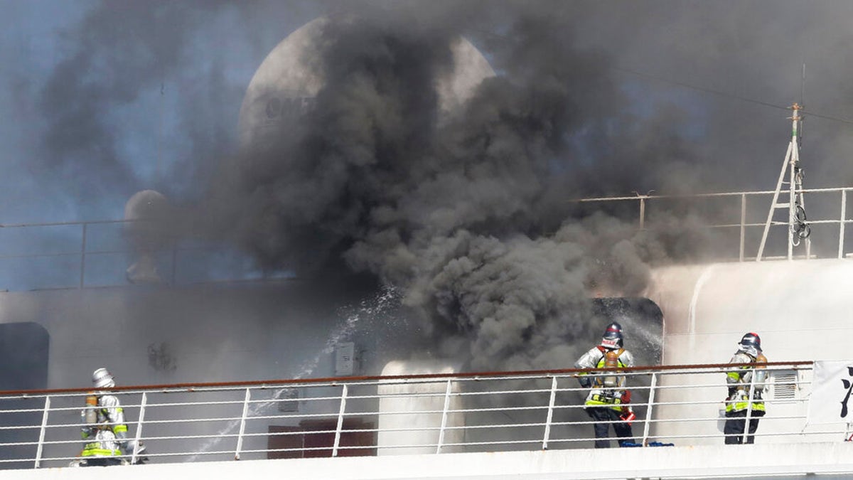 Firefighters are seen battling the fire as black smoke rises from the Asuka II docked at Yokohama Port, near Tokyo.
