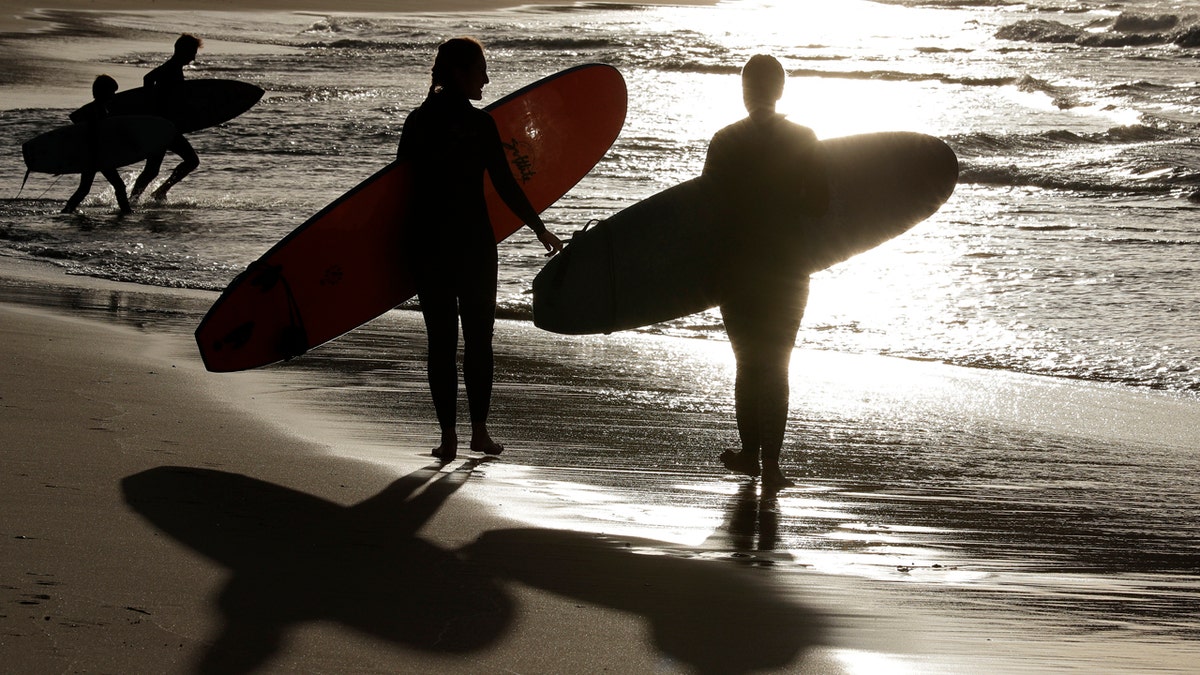 In this April 28, 2020, photo, surfers walk the beach in Sydney, Australia.