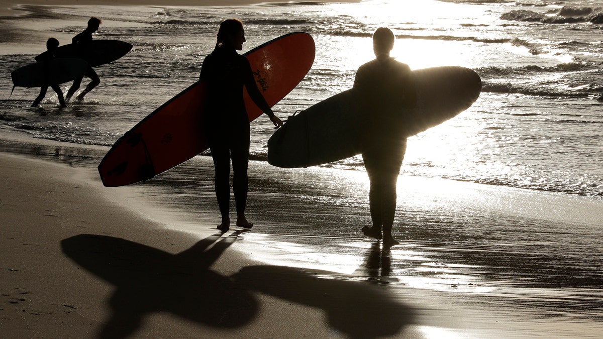 In this April 28, 2020, photo, surfers walk the beach in Sydney, Australia.
