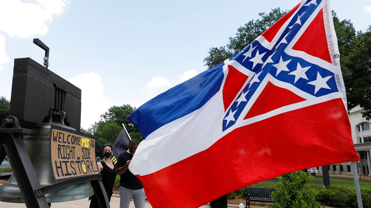 A Mississippi state flag waves adjacent to a flag change supporter's sign that welcomes the state to "the right side of history," outside the Capitol in Jackson, Miss., Sunday, June 28, 2020, while lawmakers are expected to consider state flag change legislation. Mississippi Governor Tate Reeves has already said he would sign whatever flag bill the Legislature decides on. (AP Photo/Rogelio V. Solis)
