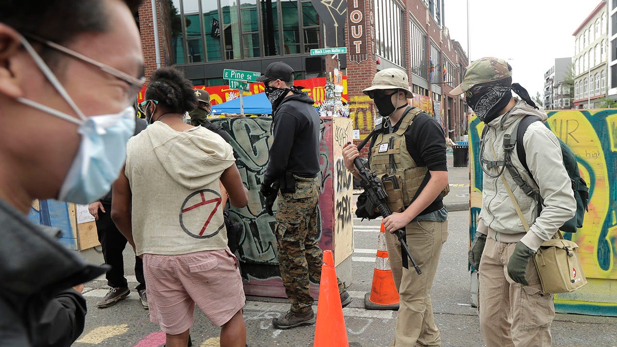 A person who said he goes by the name James Madison, second from right, carries a rifle as he walks Saturday, June 20, 2020, inside what has been named the Capitol Hill Occupied Protest zone in Seattle. Madison is part of the volunteer security team that has been working inside the CHOP zone, and said he and other armed volunteers were patrolling Saturday to keep the area safe. A pre-dawn shooting Saturday near the area left one person dead and critically injured another person, authorities said Saturday. (AP Photo/Ted S. Warren)