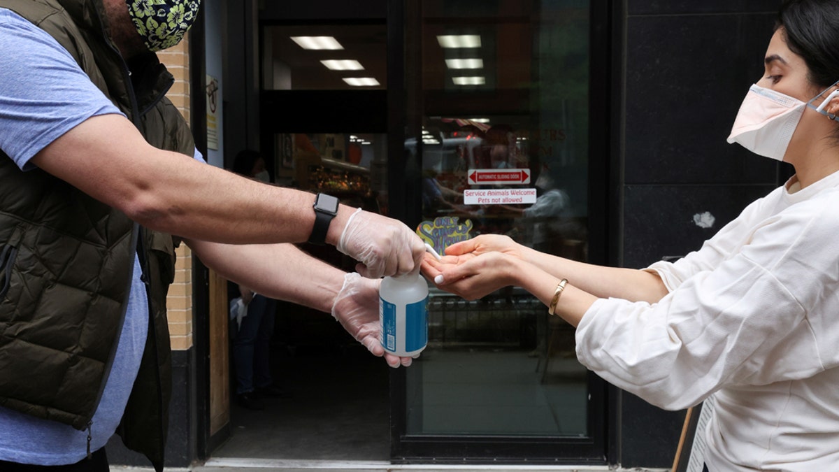 A store worker offers hand sanitizer to shoppers, during the coronavirus disease (COVID-19) outbreak, as they wait in line on the sidewalk outside a grocery store in Washington, U.S., April 14, 2020. REUTERS/Jonathan Ernst