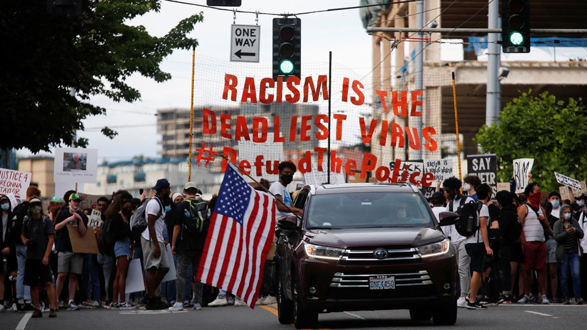 A protester sits out of the window of a car with an American flag as a youth-led protest group walks towards the Seattle Police Department's West Precinct in Seattle, Washington, U.S. June 10, 2020.?