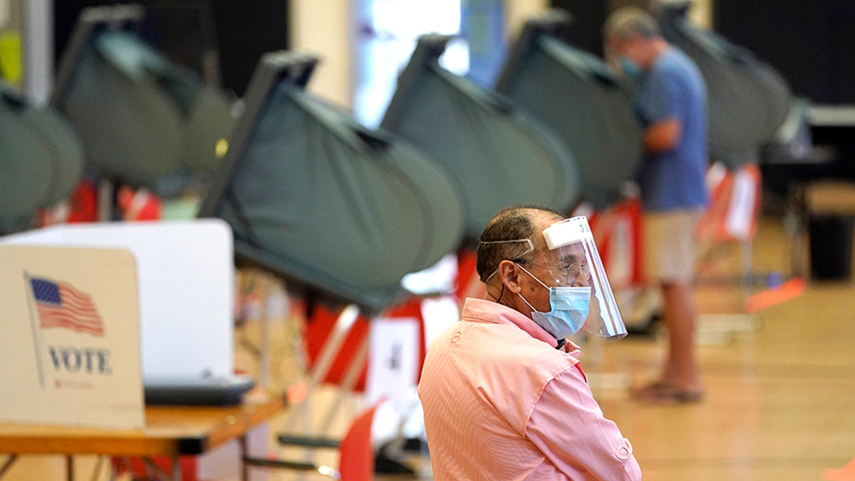 Harris County election clerk Jose Mendoza watches over voting booths, Monday, June 29, 2020, in Houston. Early voting for the Texas primary runoffs began Monday. (AP Photo/David J. Phillip)