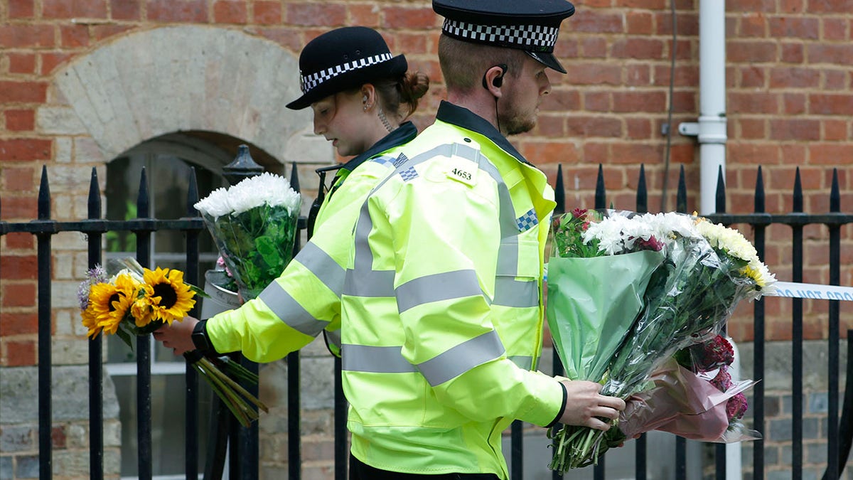 Police officers collecting flowers left at the Abbey gateway of Forbury Gardens on Sunday, one day after the stabbing attack. (AP Photo/Alastair Grant)