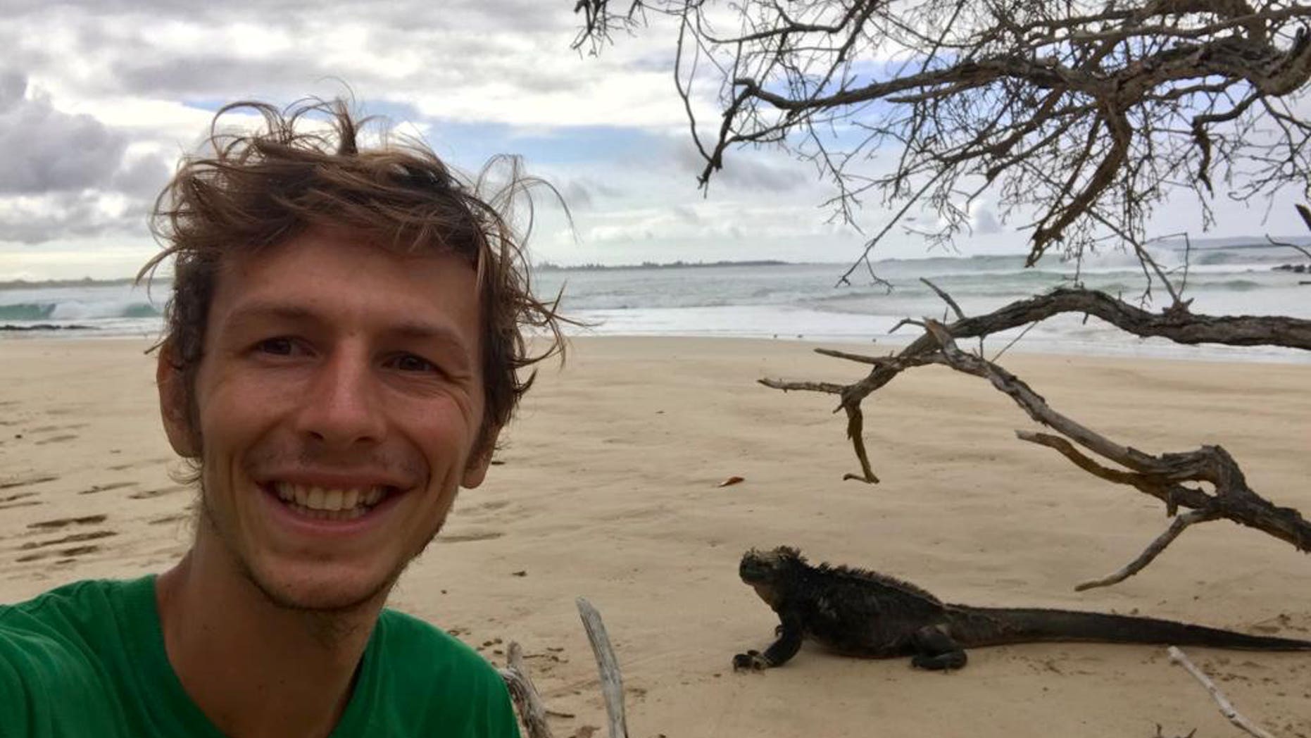 Ian Melvin berpose dengan seekor iguana di tepi pantai.