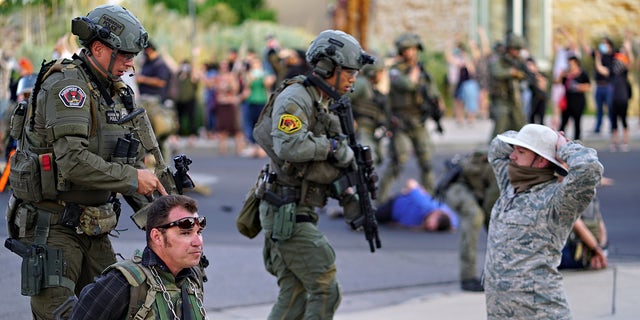 Albuquerque police detain members of the New Mexico Civil Guard, an armed civilian group, following the shooting of a man during a protest over a statue of Spanish conquerer Juan de Oñate on Monday, June 15, 2020, in Albuquerque, N.M. A confrontation erupted between protesters and a group of armed men who were trying to protect the statue before protesters wrapped a chain around it and began tugging on it while chanting: “Tear it down.” One protester repeatedly swung a pickax at the base of the statue. Moments later a few gunshots could be heard down the street and people started yelling that someone had been shot. (Adolphe Pierre-Louis/The Albuquerque Journal via AP)