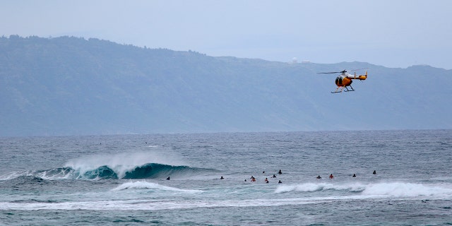 A fire and rescue helicopter flies over a group of surfers on Oahu's North Shore near Haleiwa, Hawaii on March 31, 2020. (AP Photo/Caleb Jones,File)