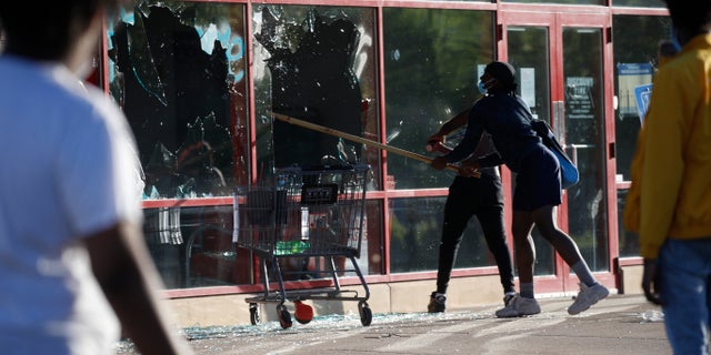 A man breaks a window at a tire store Thursday, May 28, 2020, in St. Paul, Minn. Minnesota Gov. Tim Walz called in the National Guard on Thursday as looting broke out in St. Paul and a wounded Minneapolis braced for more violence after rioting over the death of George Floyd, a handcuffed black man in police custody, reduced parts of one neighborhood to a smoking shambles. (AP Photo/John Minchillo)