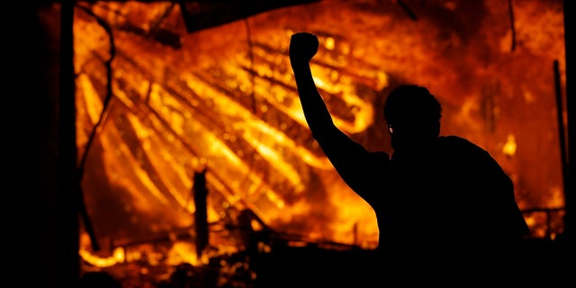 A protester gestures in front of the burning 3rd Precinct building of the Minneapolis Police Department on May 28, in Minneapolis. A suspect has been charged in connection with the suspected arson. (AP Photo/Julio Cortez)
