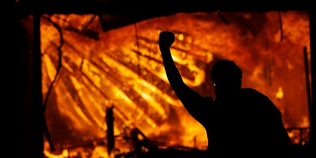 A protester gestures in front of the burning 3rd Precinct building of the Minneapolis Police Department on May 28, in Minneapolis. A suspect has been charged in connection with the suspected arson. (AP Photo/Julio Cortez)