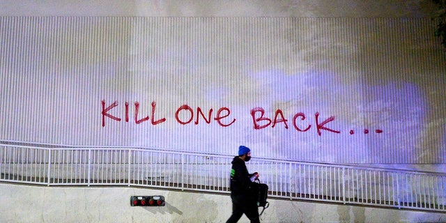 A demonstrator passes graffiti in Oakland, Calif. while protesting the death of George Floyd. (AP Photo/Noah Berger)