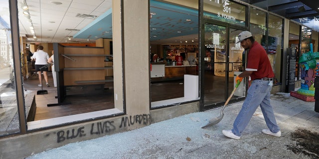 A worker sweeps broken glass from a window at the Louisville Visitors Center, early Saturday, May 30, 2020, in Louisville, Ky. The window was broken Friday evening during a protest over the deaths of George Floyd and Breonna Taylor. (AP Photo/Darron Cummings)
