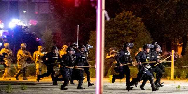 Police and Kentucky National Guard troops chase protesters as they flee toward a fence Sunday, May 31, 2020, in a parking lot at the corner of East Broadway and South Brook Street in downtown Louisville, Kentucky. (Max Gersh/The Courier Journal via AP)
