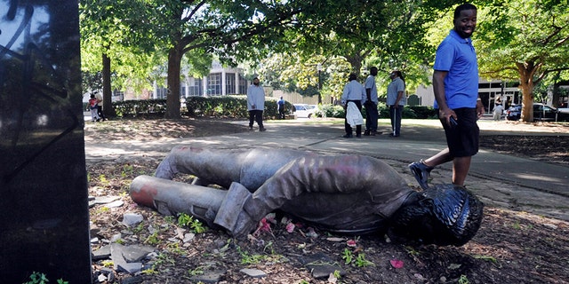 An unidentified man walks past a toppled statue in Birmingham, Ala., on Monday, June 1, 2020, following a night of unrest. People shattered windows, set fires and damaged monuments in a downtown park after a protest against the death of George Floyd. Floyd died after being restrained by Minneapolis police officers on May 25. (AP Photo/Jay Reeves)