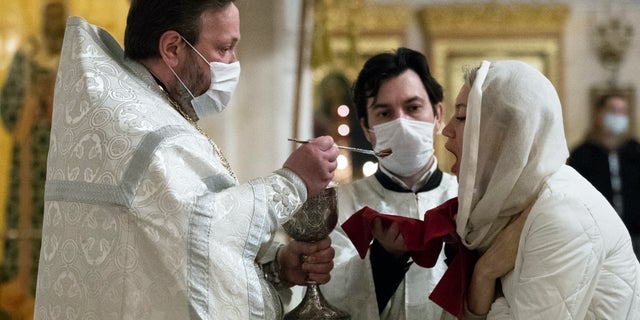 An Orthodox priest wearing a face mask to protect against coronavirus distributes Holy Communion during a service at the Christ the Savior Cathedral in Moscow, Russia, Tuesday, June 2, 2020. Churches in Moscow reopen to believers after a two-month lockdown imposed to control the spread of the coronavirus. (AP Photo/Pavel Golovkin)