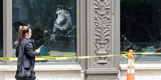 A woman walks past broken windows, Tuesday, June 2, 2020, in downtown Cleveland. The City of Cleveland extended its curfew through Tuesday night after riots broke out on Saturday over the death of George Floyd. (AP Photo/Tony Dejak)