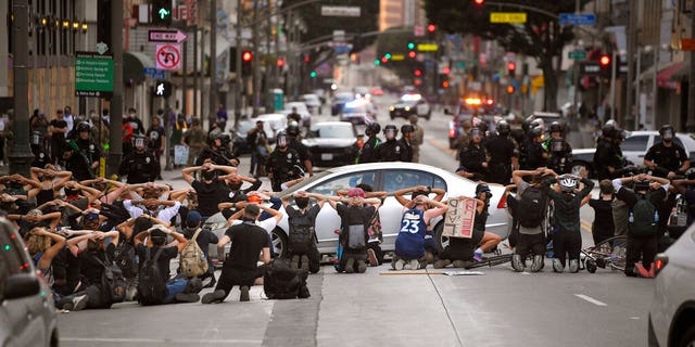 Demonstrators put their hands behind their heads before being taken into custody after the city's curfew went into effect following a protest, Tuesday, June 2, 2020, in Los Angeles over the death of George Floyd.