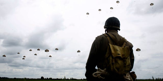 FILE - In this Wednesday, June 5, 2019 file photo, a WWII enthusiast watches French and British parachutists jumping during a commemorative parachute jump over Sannerville, Normandy, France. In sharp contrast to the 75th anniversary of D-Day, this year's 76th will be one of the loneliest remembrances ever, as the coronavirus pandemic is keeping nearly everyone from traveling. (AP Photo/Thibault Camus, File)