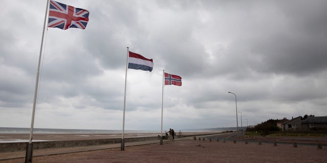In this photo taken on Thursday, June 4, 2020, two people stop to look at an information board at Omaha Beach in Saint-Laurent-sur-Mer, Normandy, France. In sharp contrast to the 75th anniversary of D-Day, this year's 76th will be one of the loneliest remembrances ever, as the coronavirus pandemic is keeping nearly everyone from traveling. (AP Photo/Virginia Mayo)