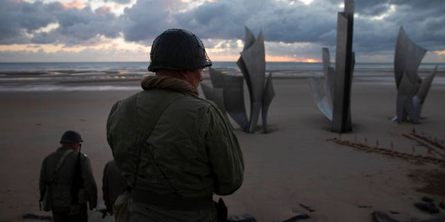 Two men in vintage US WWII uniforms walk toward the Les Braves monument at sunrise prior to a D-Day 76th anniversary ceremony in Saint Laurent sur Mer, Normandy, France, Saturday, June 6, 2020. Due to coronavirus measures many ceremonies and memorials have been cancelled in the region with the exception of very small gatherings.