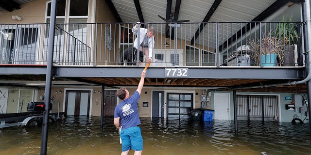 Rudy Horvath handing a piece of wood up to his wife, Dawn Horvath, as their home, a boathouse in the West End section of New Orleans, took on water from storm surge in Lake Pontchartrain on Sunday.