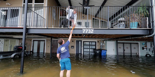 Rudy Horvath handing a piece of wood up to his wife, Dawn Horvath, as their home, a boathouse in the West End section of New Orleans, took on water from storm surge in Lake Pontchartrain on Sunday.