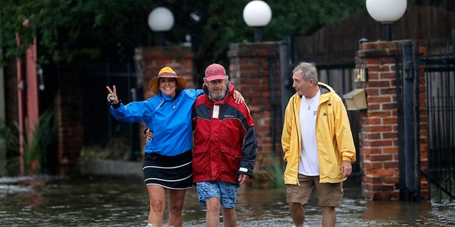 Isabelle Schneidau, left, gesturing to the camera as she walked in a rising storm surge with Mont Echols, center, and L.G. Sullivan, right, after checking on their boats in the West End section of New Orleans on Sunday.