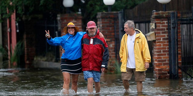 Isabelle Schneidau, left, gesturing to the camera as she walked in a rising storm surge with Mont Echols, center, and L.G. Sullivan, right, after checking on their boats in the West End section of New Orleans on Sunday.