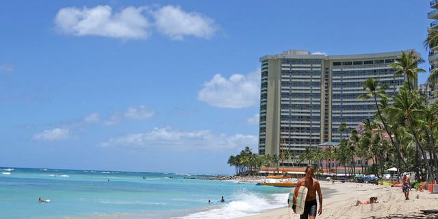 In this photo taken Friday, June 5, 2020, a surfer walks on a sparsely populated Waikiki beach in Honolulu. (AP Photo/Audrey McAvoy)