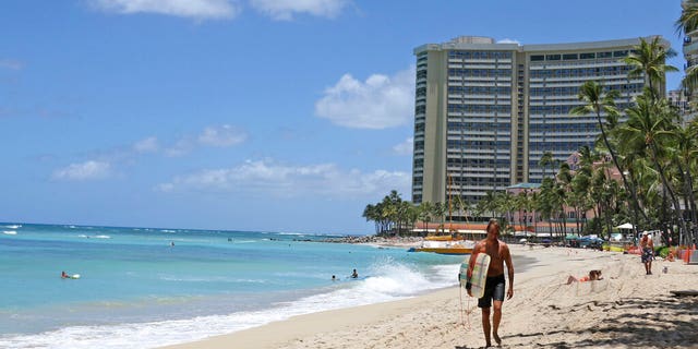 In this photo taken Friday, June 5, 2020, a surfer walks on a sparsely populated Waikiki beach in Honolulu.