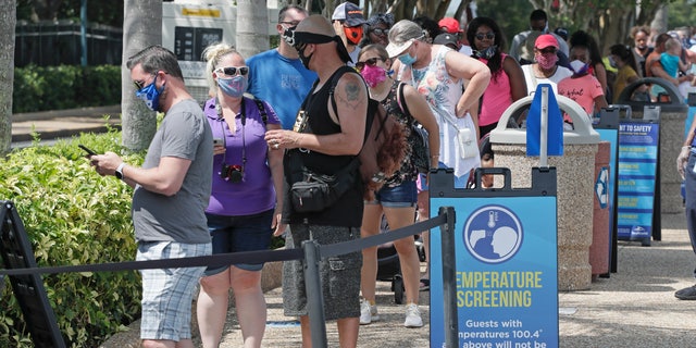 Guests wait in line to have their temperature taken before entering SeaWorld as it reopens with new safety measures in place, Thursday, June 11, 2020, in Orlando, Fla. The park had been closed since mid-March to stop the spread of the coronavirus. (AP Photo/John Raoux)