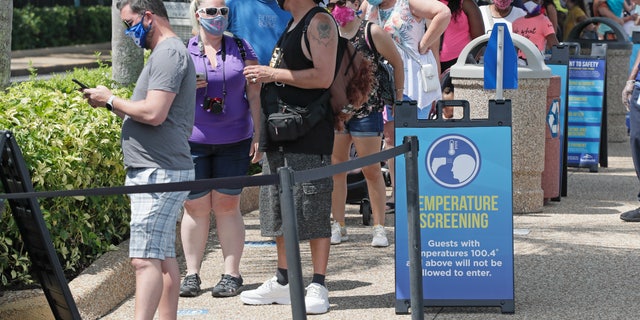 Guests wait in line to have their temperature taken before entering SeaWorld as it reopens with new safety measures in place, Thursday, June 11, 2020, in Orlando, Fla. The park had been closed since mid-March to stop the spread of the coronavirus. (AP Photo/John Raoux)