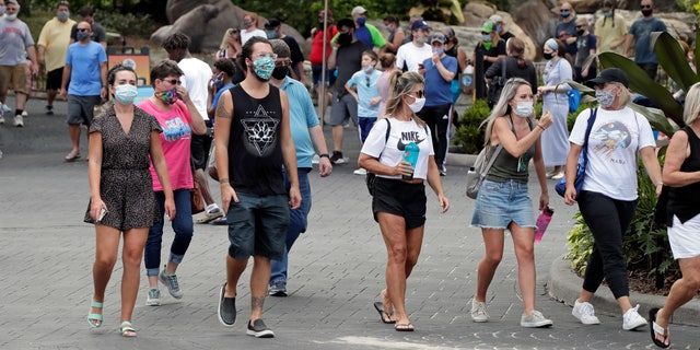Guests wearing masks stroll through SeaWorld as it reopened with new safety measures in place Thursday, June 11, 2020, in Orlando, Fla. (AP Photo/John Raoux)