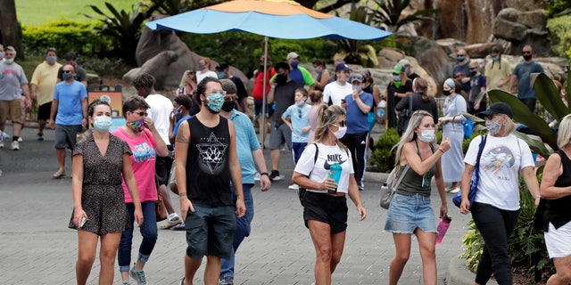 Guests wearing masks stroll through SeaWorld as it reopened with new safety measures in place Thursday, June 11, 2020, in Orlando, Fla. (AP Photo/John Raoux)