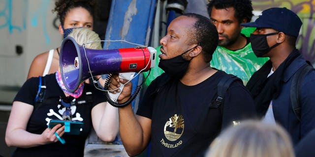 Mark Henry Jr., center, a Black Lives Matter leader, speaks into a megaphone in a doorway of the Seattle Police Department East Precinct building, which has been boarded up and abandoned except for a few officers inside, Thursday, June 11, 2020, in Seattle. 