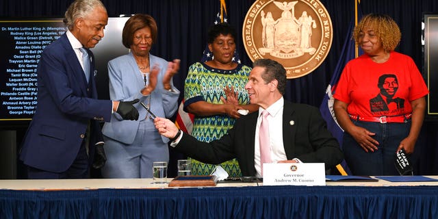 New York Governor Andrew M. Cuomo, center, hands a pen to Rev. Al Sharpton after signing into law, Friday, June 12, 2020, in New York, a sweeping package of police accountability measures that received new backing following protests of George Floyd's killing. (Kevin P. Coughlin, Office of New York Governor Andrew M. Cuomo via AP)