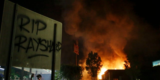 "RIP Rayshard" is spray painted on a sign as as flames engulf a Wendy's restaurant during protests Saturday, June 13, 2020, in Atlanta. The restaurant was where Rayshard Brooks was shot and killed by police Friday evening following a struggle in the restaurant's drive-thru line. (AP Photo/Brynn Anderson)