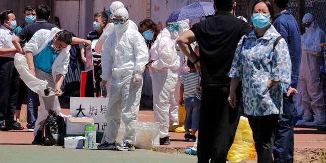 Workers put on protective suits as they wait for people living surrounding the Xinfadi wholesale market arrive to get a nucleic acid test at a stadium in Beijing, Sunday, June 14, 2020. China is reporting its highest daily total of coronavirus cases in two months after the capital's biggest wholesale food market was shut down following a resurgence in local infections. (AP Photo/Andy Wong)