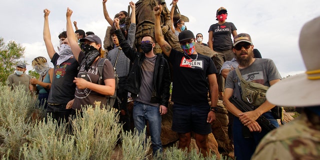 Demonstrators climb the statue of Don Juan de Onate in Old Town in Albuquerque, N.M., while an armed member of the New Mexico Civil Guard stands by during a protest calling for the removal of the likeness of the controversial New Mexico explorer Monday, June 15, 2020. (Adolphe Pierre-Louis/The Albuquerque Journal via AP)