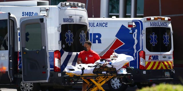 A person is brought to a medical transport vehicle from Banner Desert Medical Center as several transports and ambulances are shown parked outside the emergency room entrance, June 16, in Mesa, Ariz.