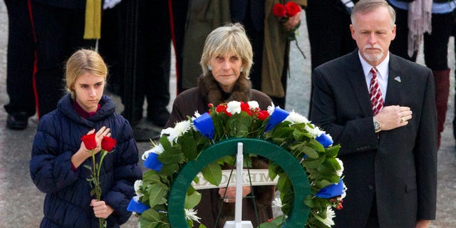 FILE - In this Nov. 22, 2013 file photo, An unidentified girl, left, holds a rose during a wreath laying ceremony with former Ambassador to Ireland Jean Kennedy Smith, center, and Patrick Hallinan, executive director of Army National Military Cemeteries, at the grave of John F. Kennedy at Arlington National Cemetery, in Arlington, Va. Jean Kennedy Smith, the youngest sister and last surviving sibling of President John F. Kennedy, died at 92, her daughter confirmed to The New York Times, Wednesday, June 17, 2020. (AP Photo/Jacquelyn Martin)