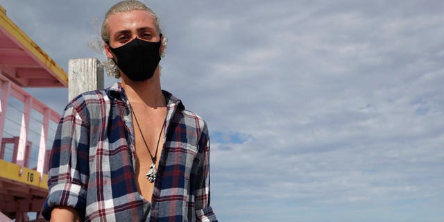 Nivek Divincci wears a protective mask as he poses for a photograph on the beach at Haulover Park during the new coronavirus pandemic, Friday, June 19, 2020, in Miami. 