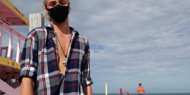 Nivek Divincci wears a protective mask as he poses for a photograph on the beach at Haulover Park during the new coronavirus pandemic, Friday, June 19, 2020, in Miami. 