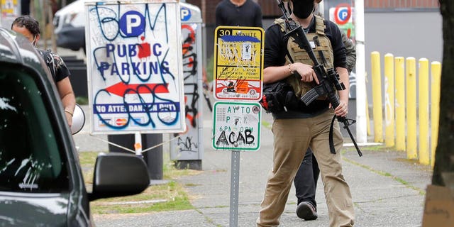 A person who said he goes by the name James Madison carries a rifle as he walks June 20, 2020, near what has been named the Capitol Hill Occupied Protest zone in Seattle. Madison is part of the volunteer security team who have been working inside the CHOP zone, and said he and other armed volunteers were patrolling Saturday to keep the area safe. (AP Photo/Ted S. Warren)