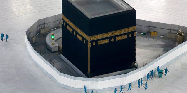 In this March 7, 2020 file photo, workers disinfect the ground around the Kaaba, the cubic building at the Grand Mosque, in the Muslim holy city of Mecca, Saudi Arabia after authorities emptied Islam's holiest site for sterilization over fears of the new coronavirus. (AP Photo/Amr Nabil, File)